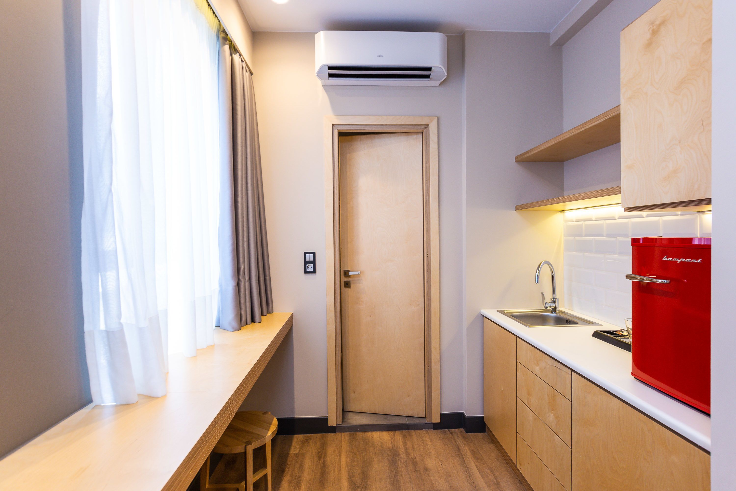 A compact kitchen with a wooden countertop, a red refrigerator, and a built-in sink.