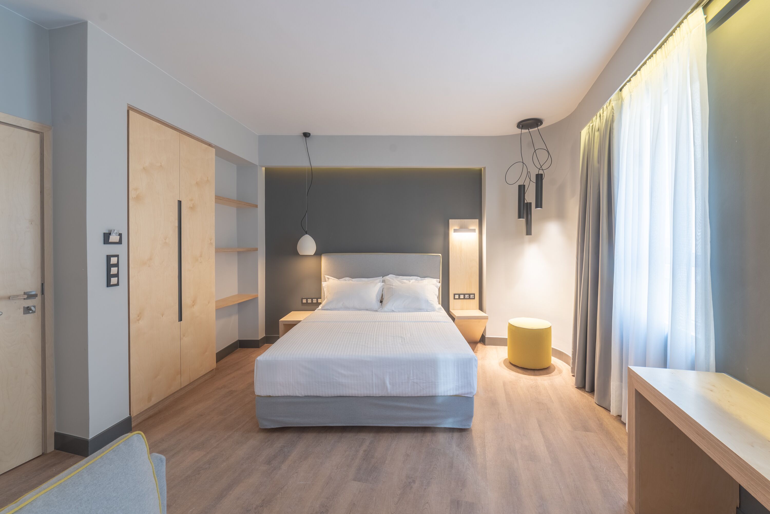 A modern bedroom with a large bed, wooden flooring, built-in wardrobe, bedside lamps, and a small round table.