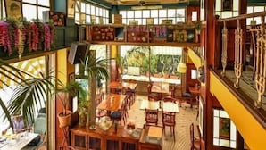 A spacious indoor area with multiple wooden tables and chairs, a ceiling fan, and a view of the outdoors through large windows. - St. Bjur Suites (Athens)