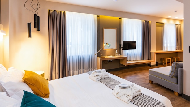 A modern hotel room with a large bed, a sofa, a desk, and a TV. - St. Bjur Suites (Athens)