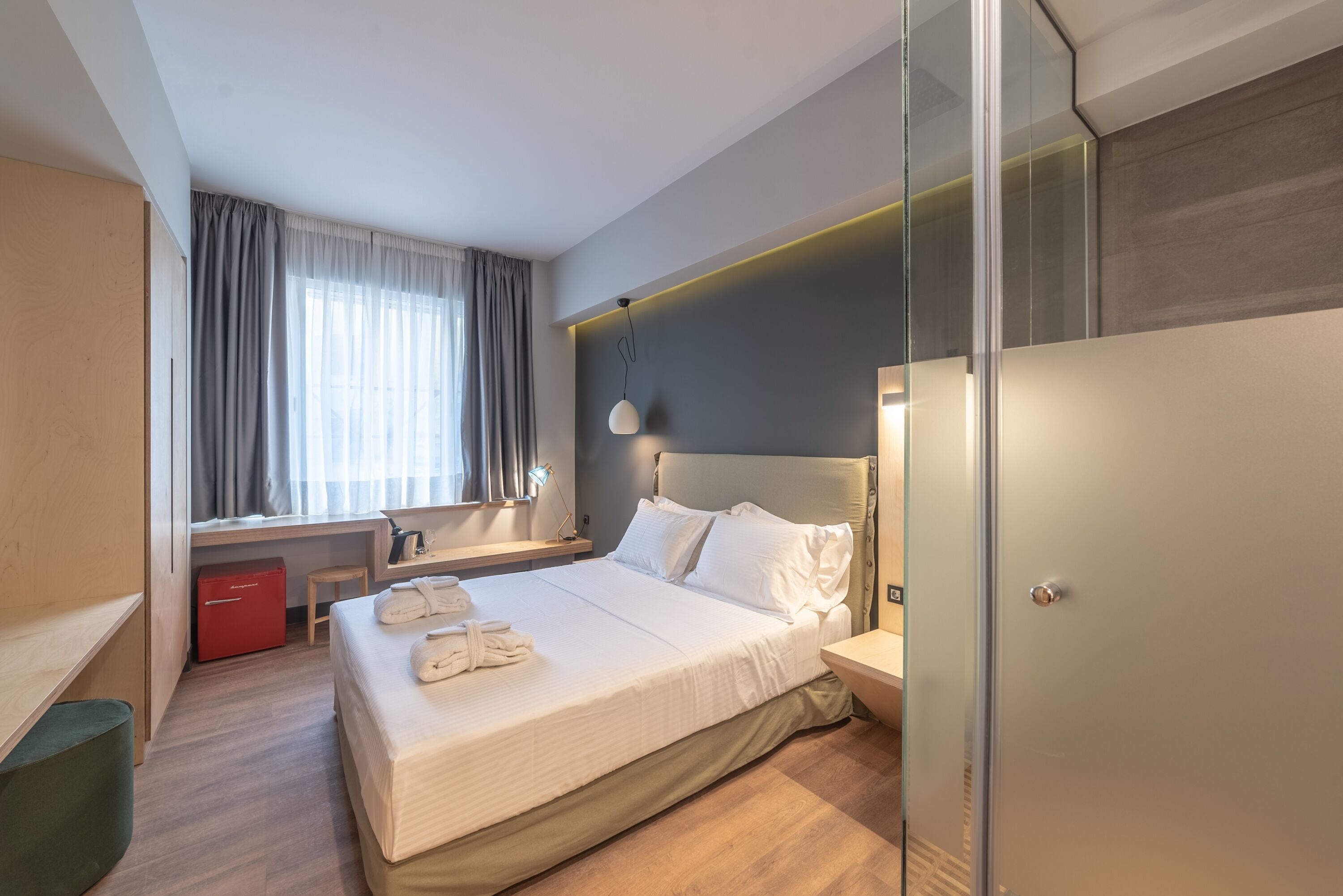 Et moderne hotelværelse med en stor seng, et skrivebord, en stol, et garderobeskab og et vindue med gardiner.