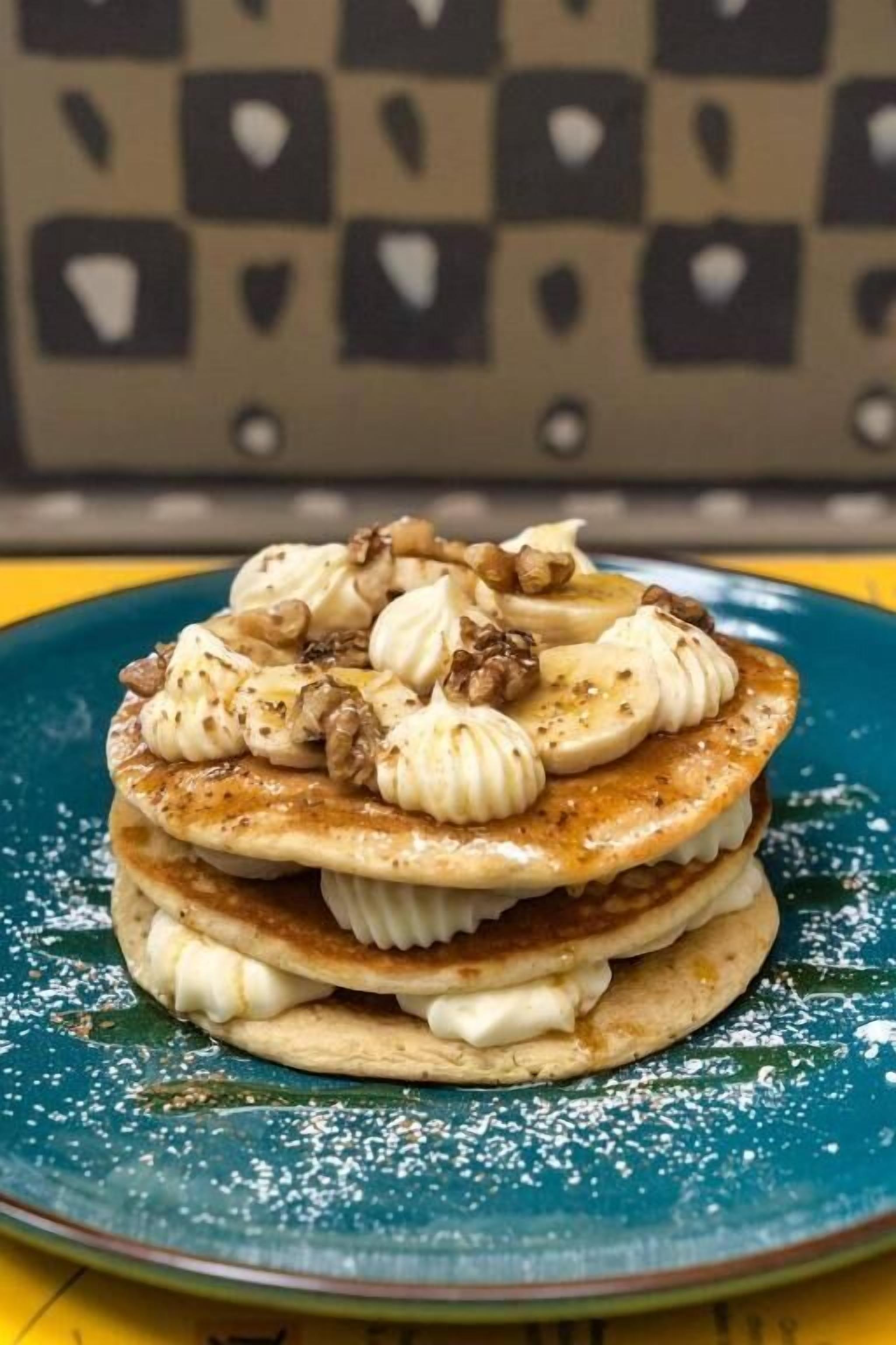 A stack of pancakes with whipped cream and walnuts on a blue plate.