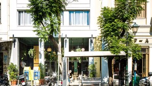 A multi-story building with a covered outdoor seating area, a row of parked motorcycles, and a clear blue sky. - St. Bjur Suites (Athens)