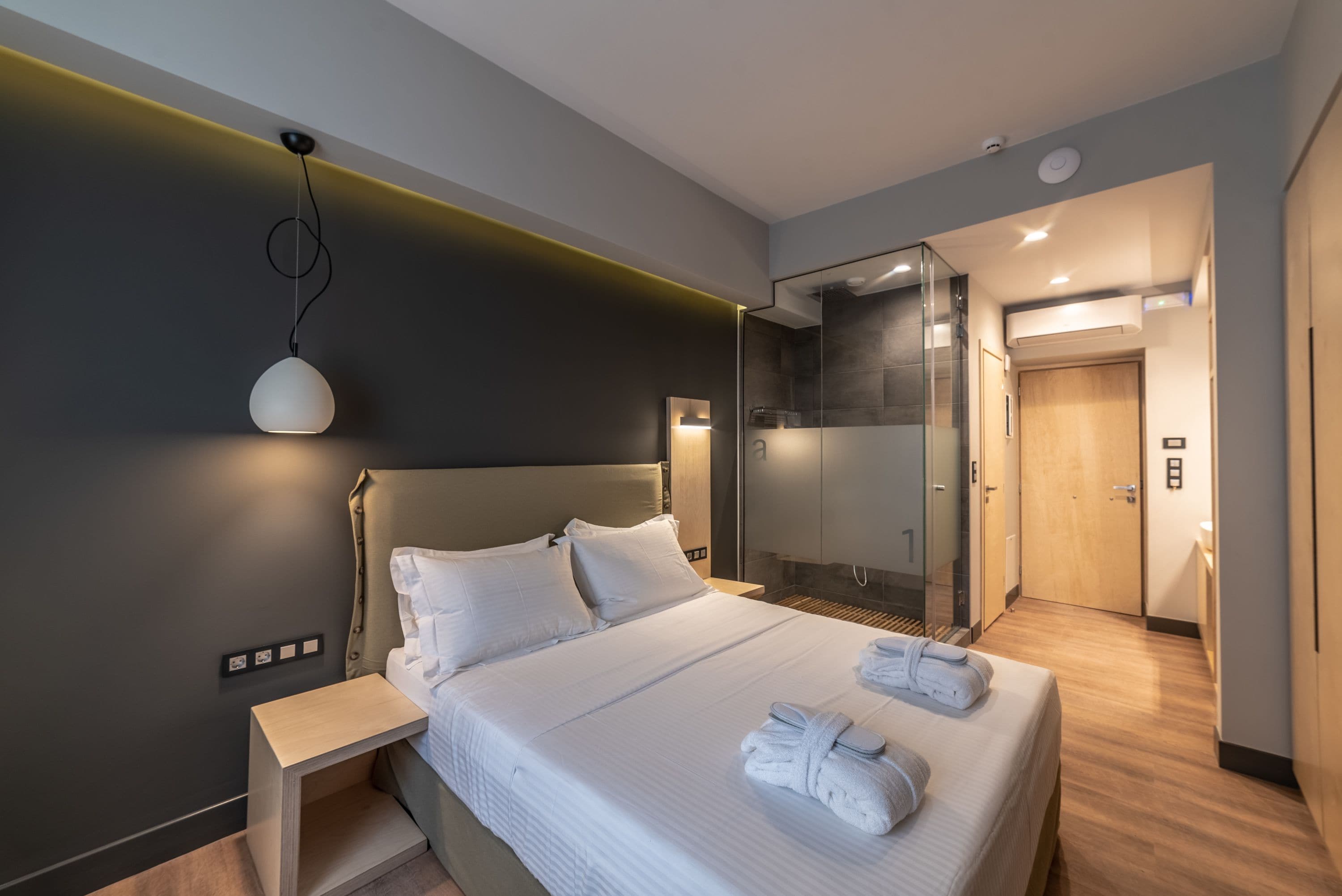 A modern hotel room with a large bed, bedside tables, a glass shower enclosure, and a visible bathroom door.