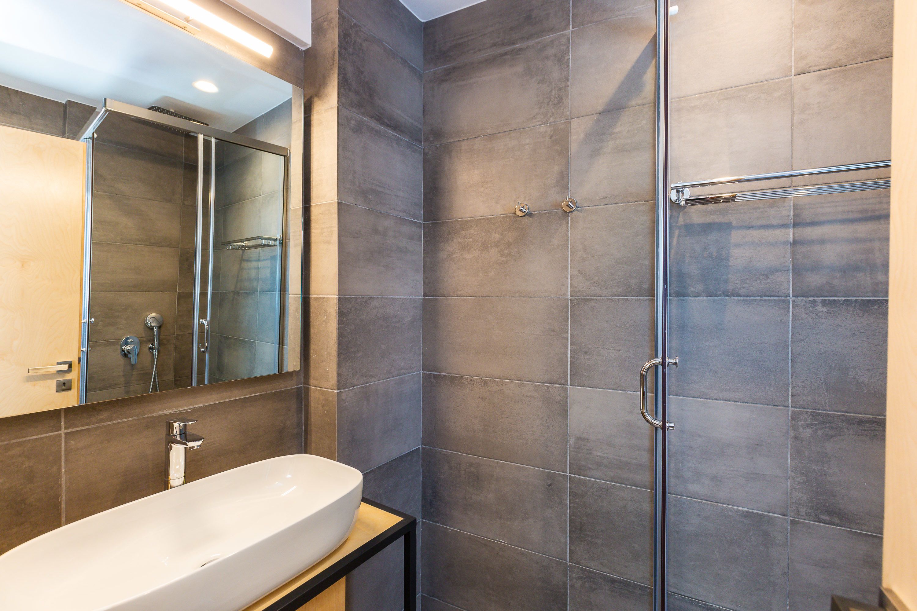 Un baño moderno con un lavamanos grande de color blanco, una cabina de ducha de vidrio y un espejo sobre el lavamanos.