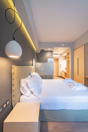 A modern hotel room with a neatly made bed, a bedside table, a wardrobe, and a bathroom visible through an open door. - St. Bjur Suites (Athens)