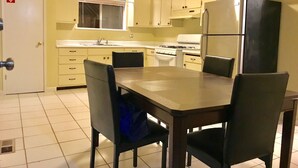 Une cuisine de taille réduite, avec des meubles blancs, une cuisinière, un réfrigérateur et une table à manger avec des chaises.