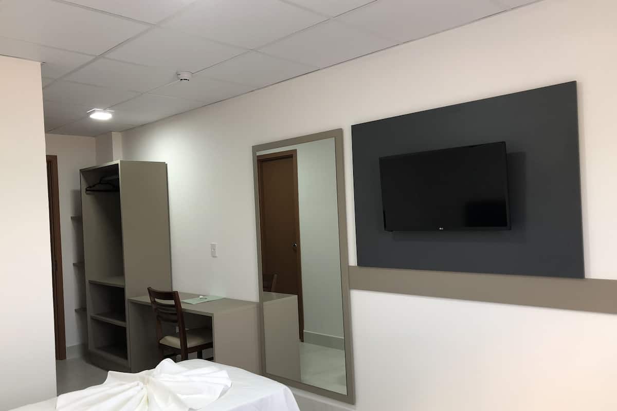 Habitación de hotel moderna con cama, escritorio, silla, armario, espejo y televisor de pantalla plana montado en la pared.