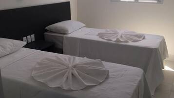 A hotel room with two single beds, each with a white bedspread and a decorative white bow on the bed. There is a window with a view of greenery outside.