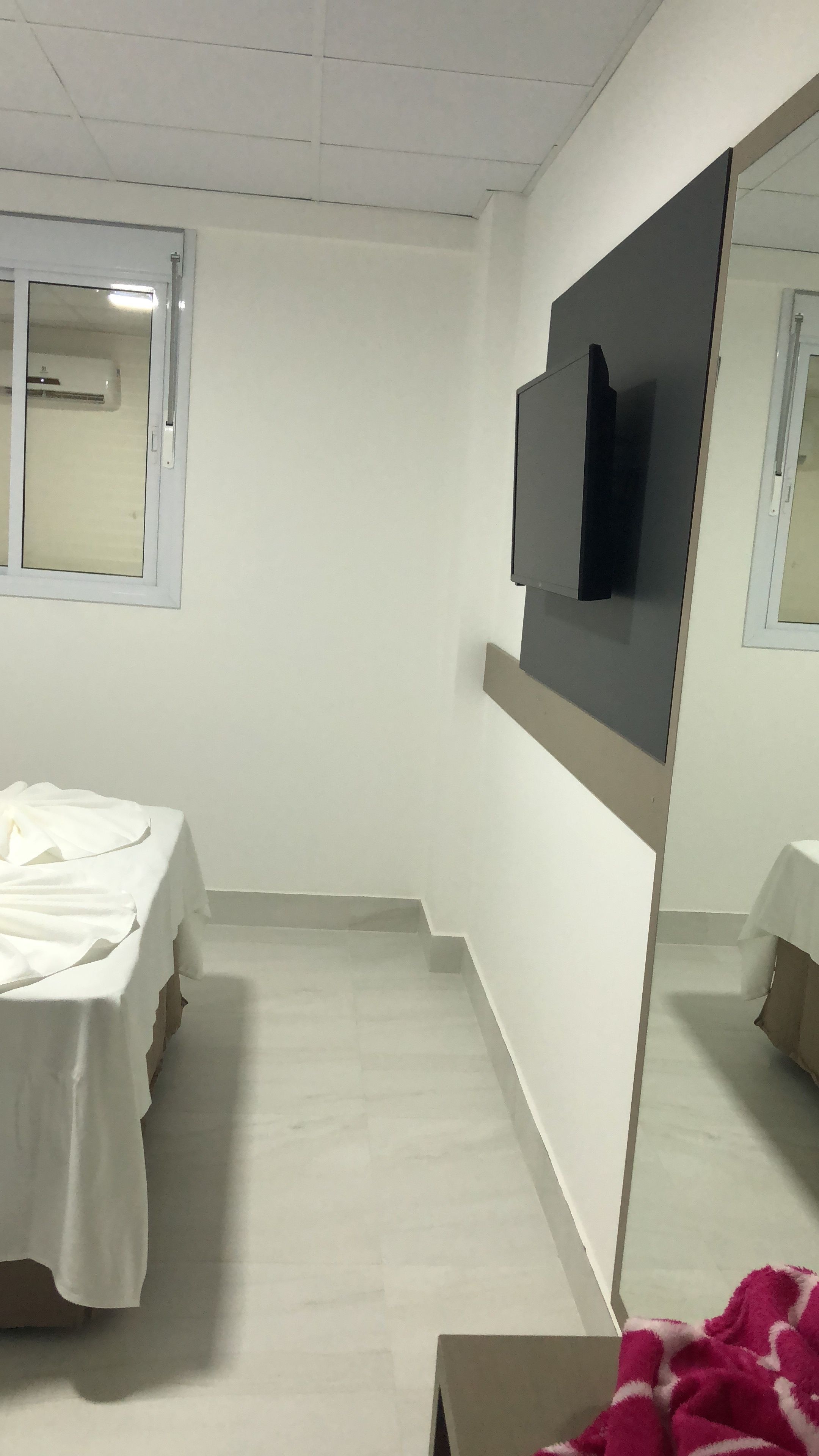 Une chambre dotée d’un lit, d’un téléviseur à écran plat fixé au mur et d’une fenêtre avec un appareil de climatisation.