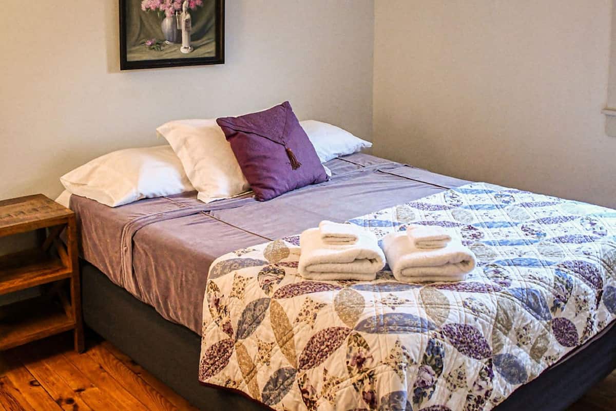 A bedroom with a bed, pillows, a blanket, a framed picture, and an air conditioning unit.