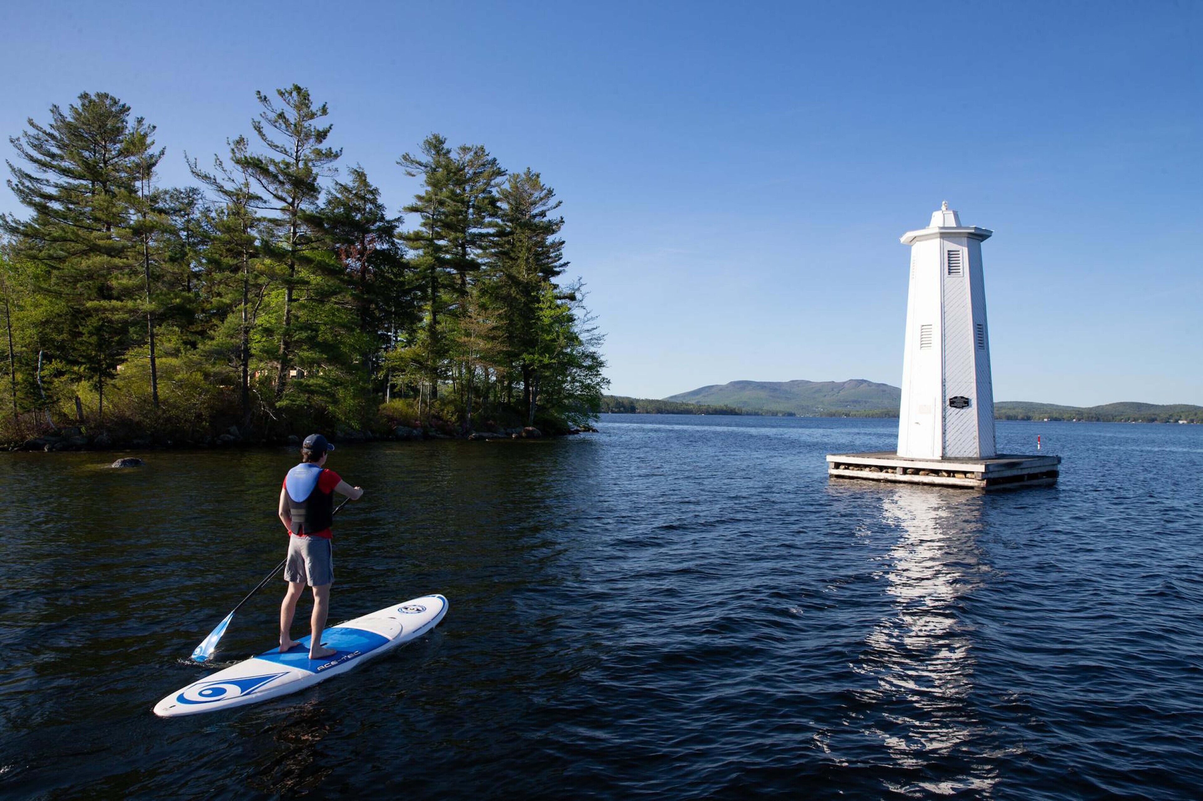 A person paddleboarding on a calm lake with a lighthouse in the background.