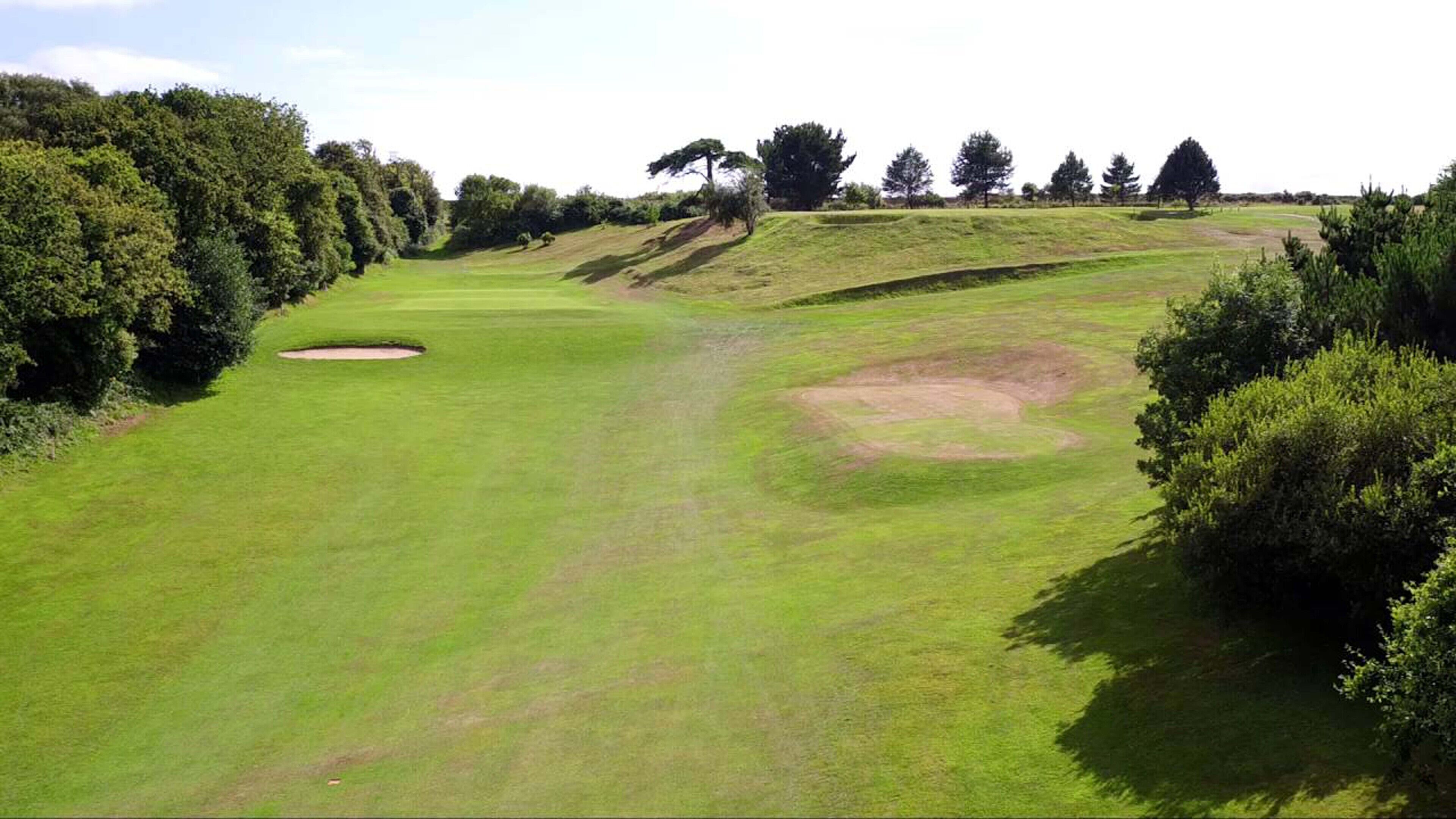 A golf course with a sand bunker, trees, and a clear sky.