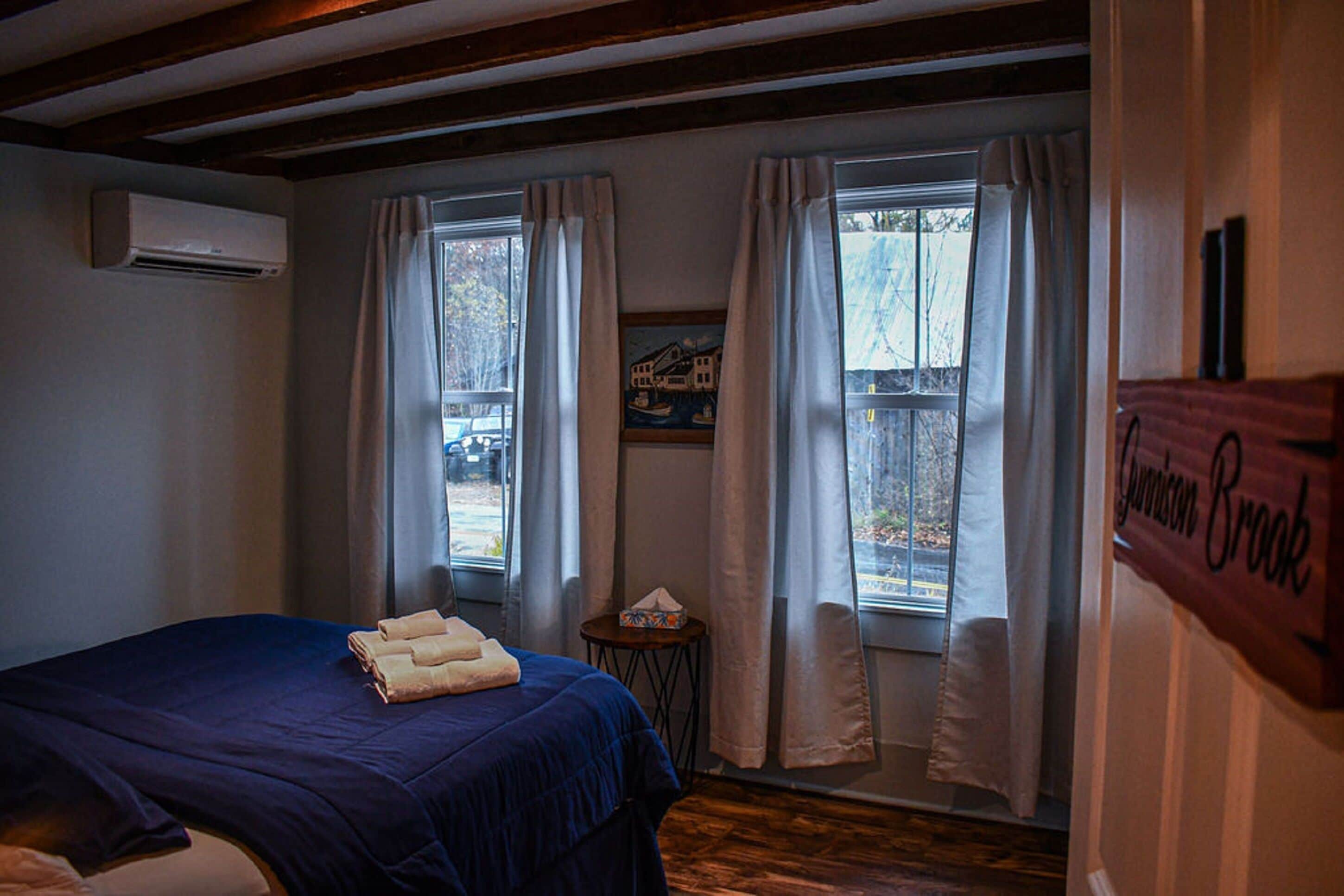 A hotel room with a bed, a small table, and a window with curtains.