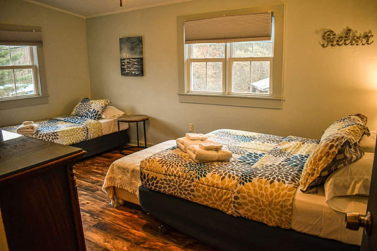 A room with two beds, a small table, and a painting on the wall.