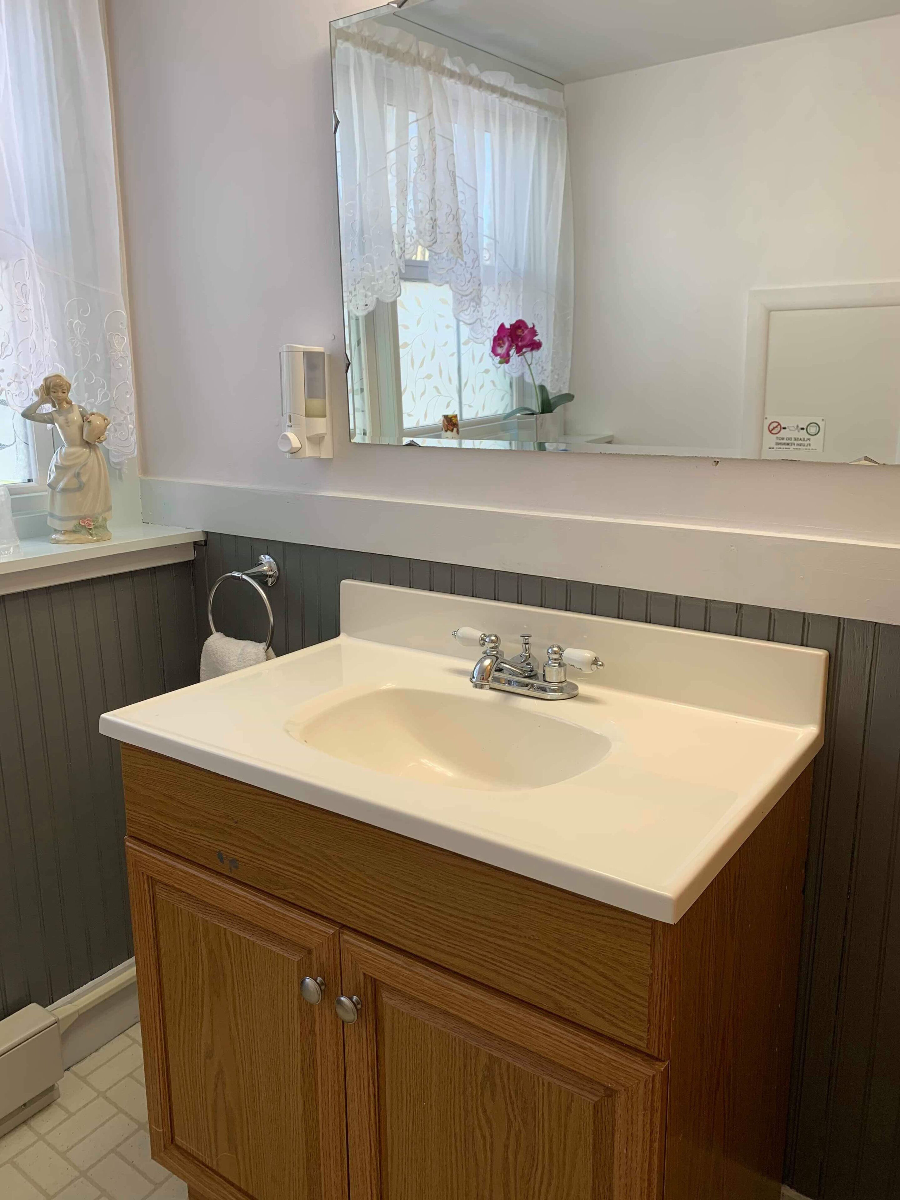 A bathroom with a white sink, wooden vanity, and a mirror above.