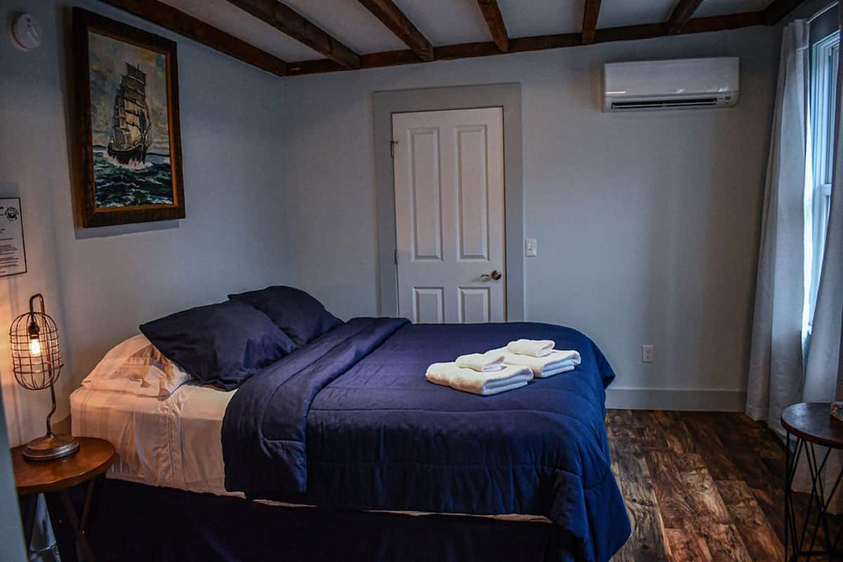 A bedroom with a bed, a door, an air conditioner, and a painting on the wall.