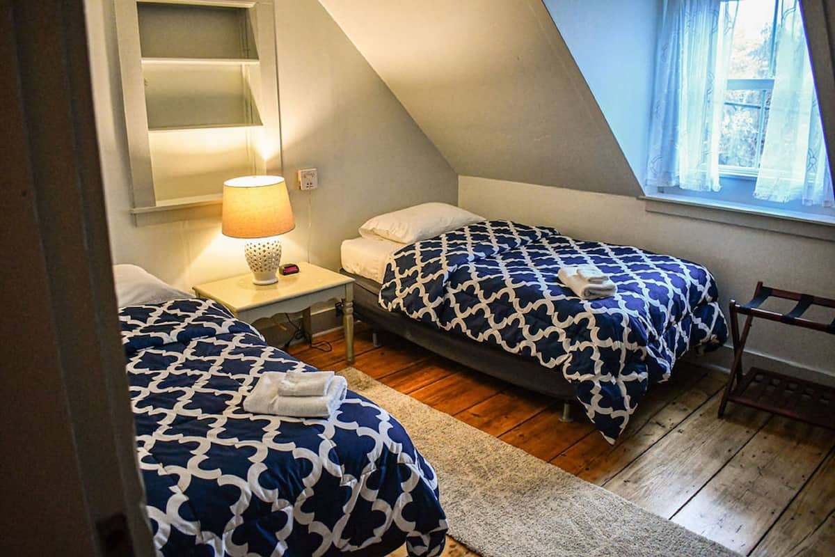 A bedroom with two beds, a nightstand, a lamp, and a window with curtains.