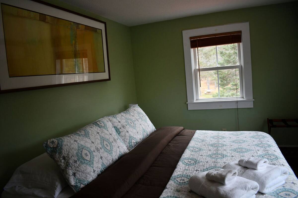 A bedroom with a bed, pillows, a window, and a painting on the wall.