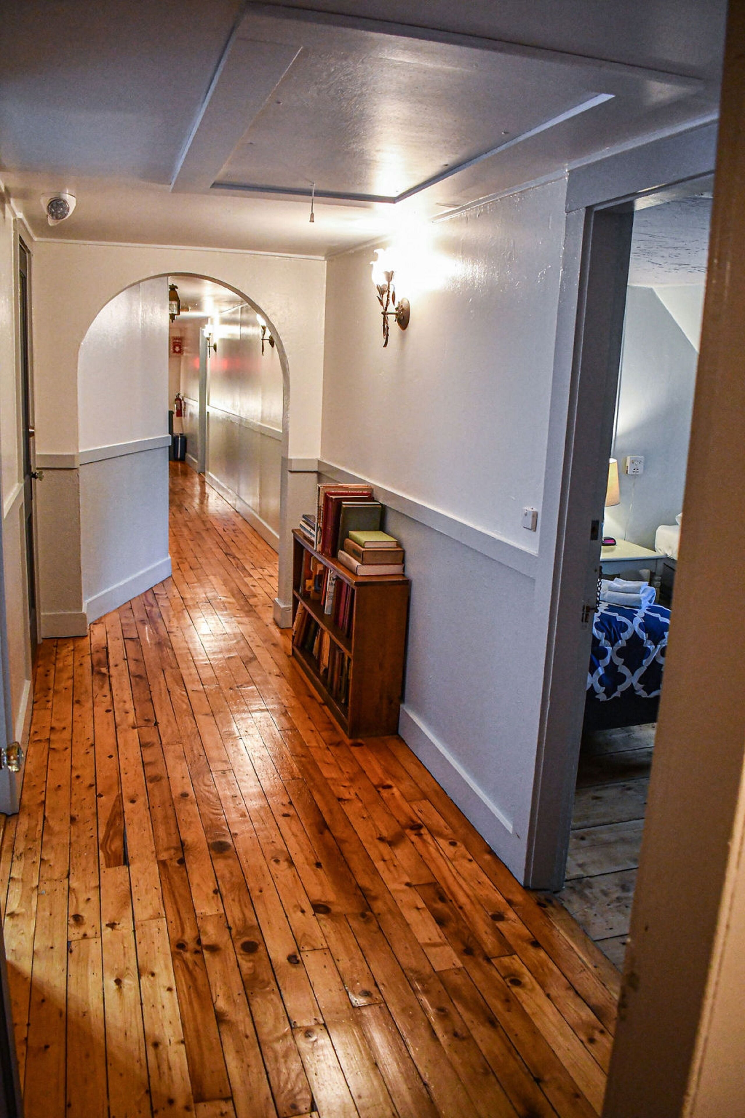 Un pasillo con piso de madera, una estantería y un acceso a otra habitación.