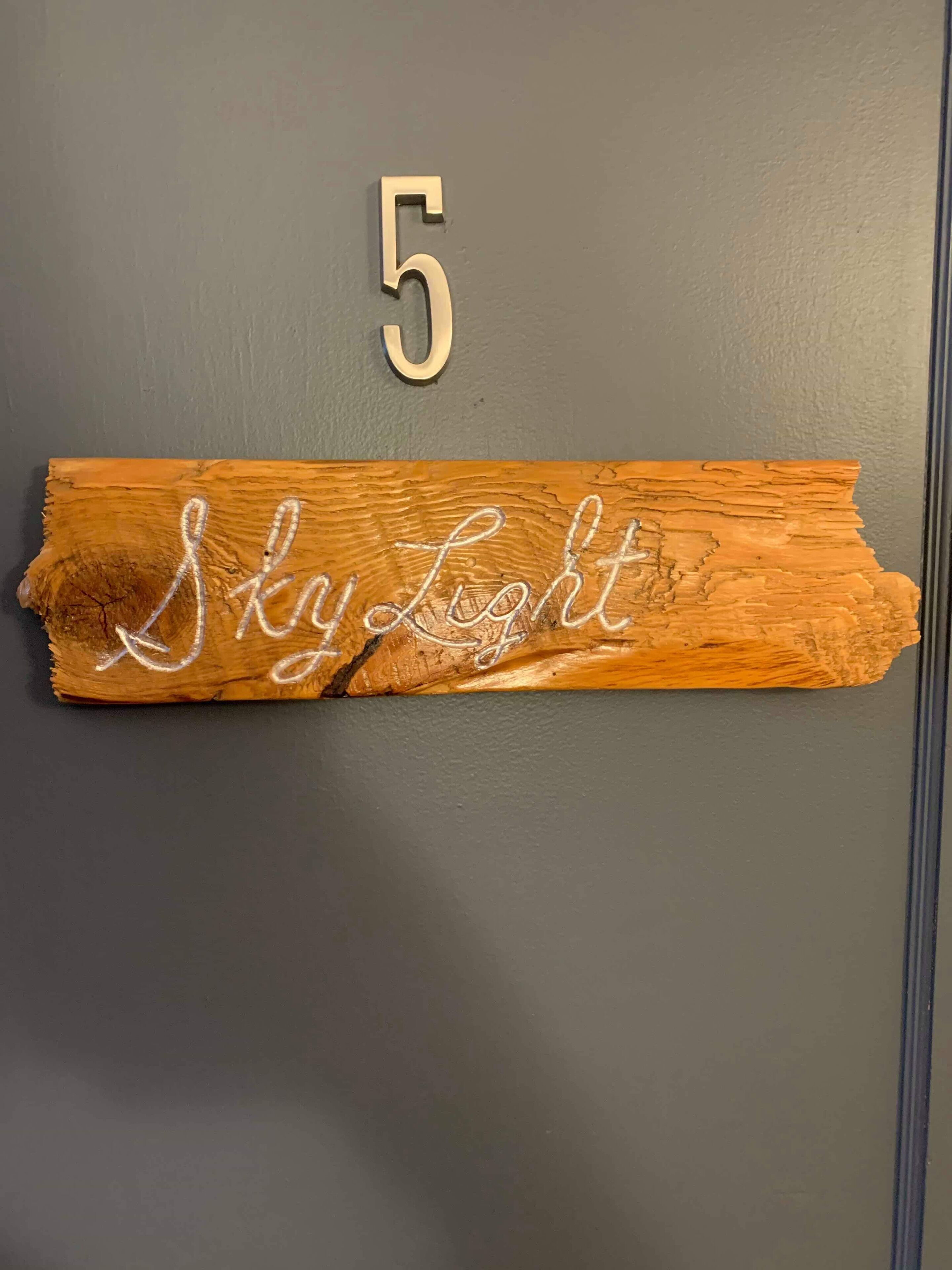 Una placa de madera con el número 5 y la inscripción 'Sky Light' en una puerta gris.