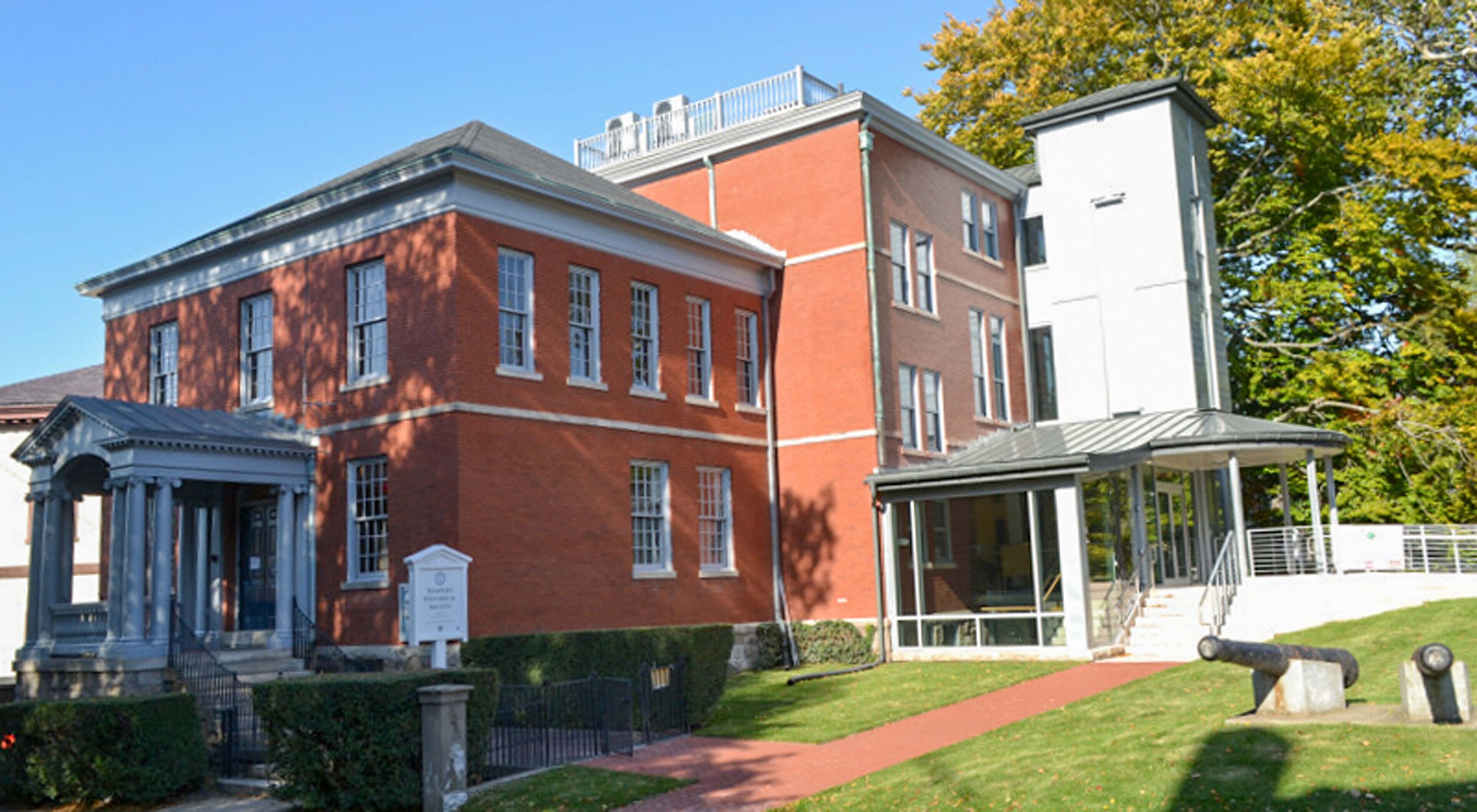 A red brick building with a classical facade, a covered walkway, and a well-maintained lawn.