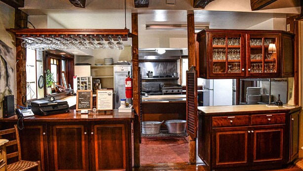 A wooden bar area with a countertop, glasses, and a chalkboard menu.