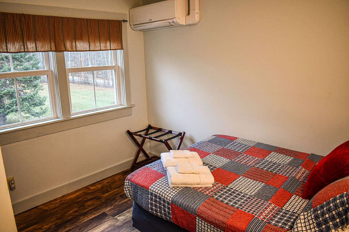A bedroom with a bed, a window, an air conditioning unit, and a wooden chair.