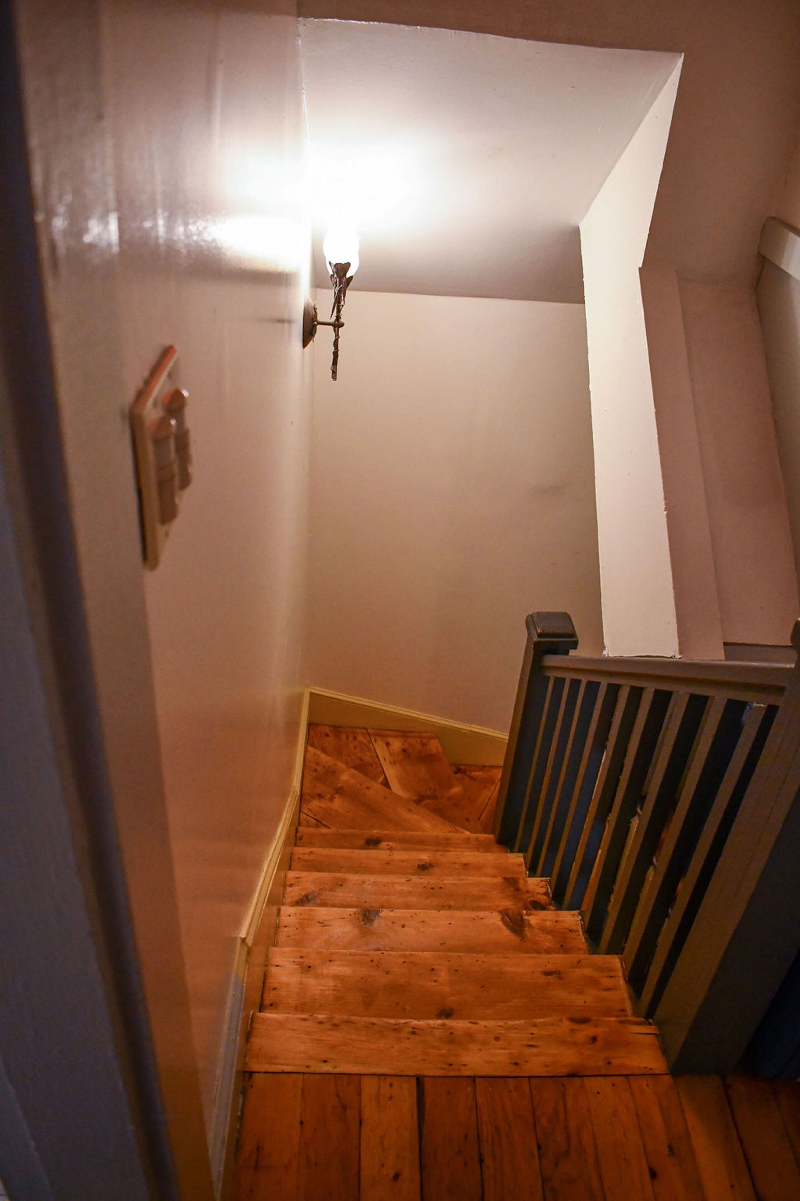 A wooden staircase with a handrail, a light fixture, and a door with a lock.