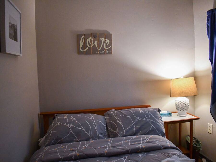 A bedroom with a bed, a bedside table with a lamp, a wall decoration, and a framed picture.