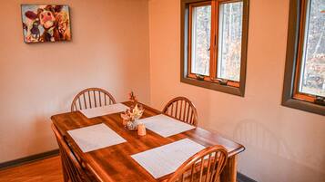 A dining room with a wooden table, four chairs, and a window with a view of trees.