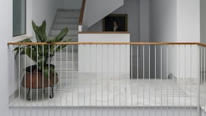 Un interior moderno con una escalera que sube a un nivel superior, una planta en maceta y una barandilla.