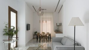 Una sala de estar moderna con un sofá gris, una mesa de centro de vidrio, una zona de comedor con una mesa y sillas, una lámpara colgante y una lámpara de pie.