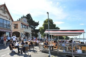 An outdoor café with tables and chairs, a covered seating area, and a view of the water. - Le Nid du Héron: An urban vacation rental with a heated pool in the heart of Nantes (Nantes)