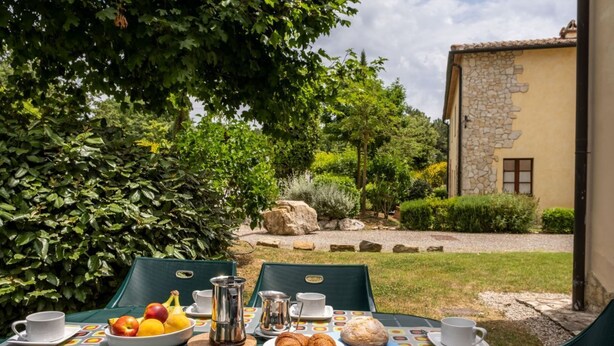 An outdoor dining area with a table set for breakfast, including croissants, bread, and fruit.