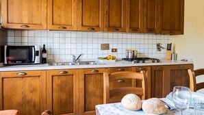 A kitchen with wooden cabinets, a microwave, a sink, a stove, and a dining table with bread and wine glasses.