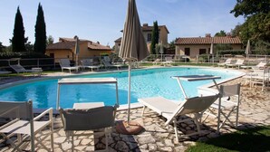 A pool area with lounge chairs and umbrellas, surrounded by stone flooring and traditional buildings.