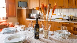 A dining table set with plates, glasses, and a bottle of wine in a kitchen with wooden cabinets and a tiled backsplash.