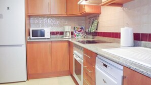 Una cocina con armarios de madera, un refrigerador blanco, un microondas, una cafetera y un escurreplatos.
