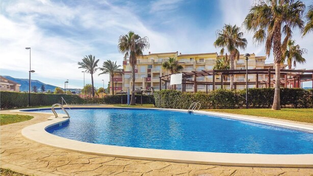 Una piscina con borde de piedra, rodeada de palmeras y un edificio con balcones al fondo.