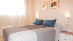 Una cama bien hecha con una colcha blanco y gris, dos almohadas color turquesa y una mesita de noche con una lámpara.