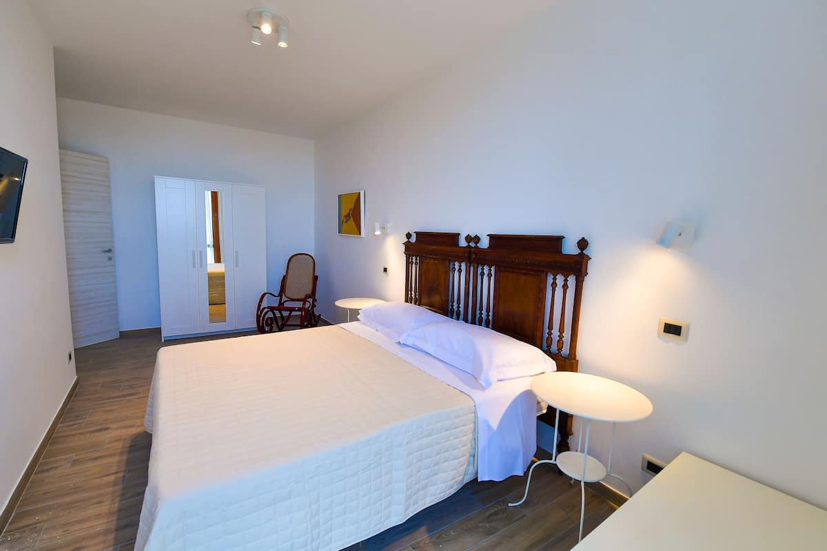 A bedroom with a large bed, a chair, a small table, and a wardrobe.