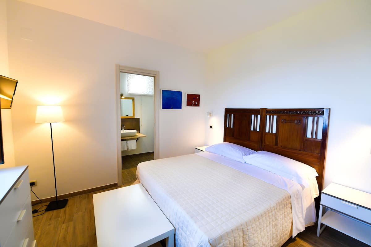 A neatly arranged bedroom with a bed, bedside table, lamp, and a view into the bathroom.