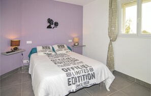 Een slaapkamer met een bed, twee nachtkastjes, een lamp op elk nachtkastje, een wandklok en een raam met gordijnen.