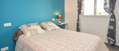 A bedroom with a bed, a nightstand, a lamp, and a window with curtains.