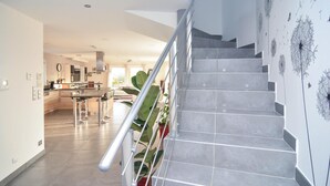 A modern kitchen with a central island, a dining area with chairs, and a staircase with a metal railing. - Lovely home in Saint-Gilles (Saint-Gilles)