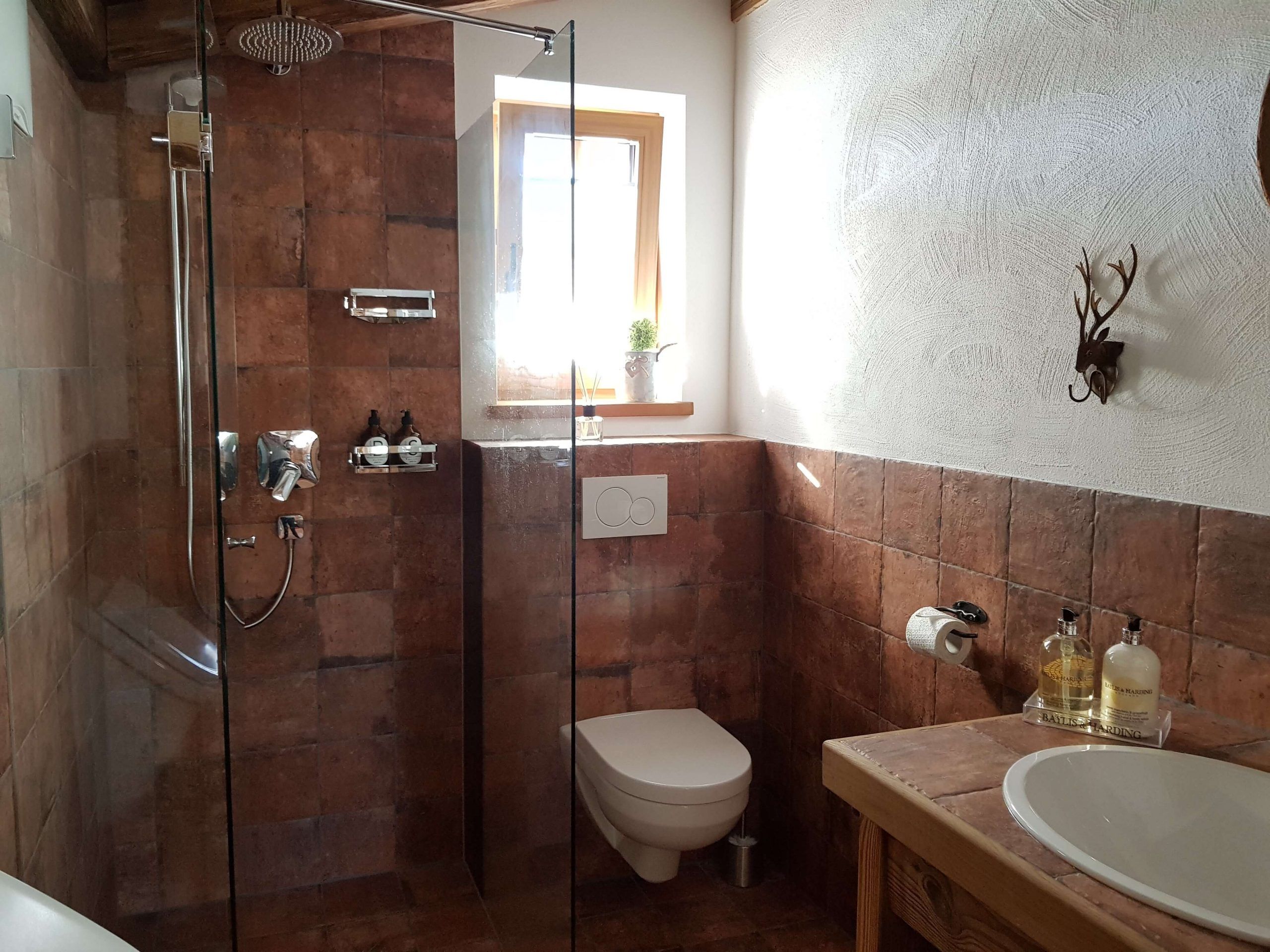 A bathroom with a glass-enclosed shower, a toilet, and a sink with toiletries.