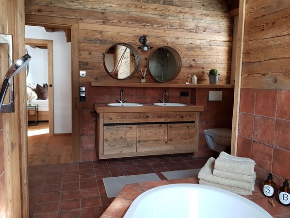 Un baño de madera con lavamanos doble, dos espejos, una bañera y un inodoro.