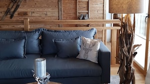 Una habitación acogedora con un sofá azul oscuro, una mesa redonda de madera y una vela, además de una lámpara.