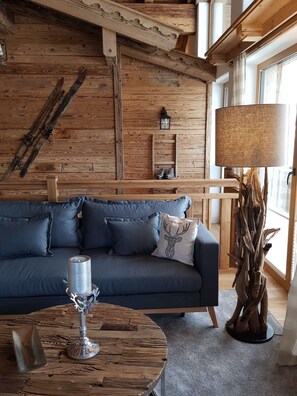Ein gemütliches Zimmer mit einem dunkelblauen Sofa, einem runden Holztisch mit Kerze und einer Lampe.